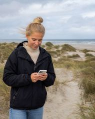 junge frau am strand in dänemark mit einem smartphone
